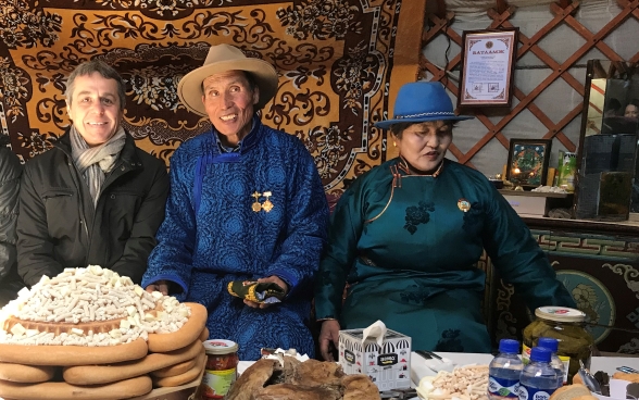 Bundesrat Cassis sitzt an einem reich gedeckten Tisch mit zwei mongolischen Viehzüchter.