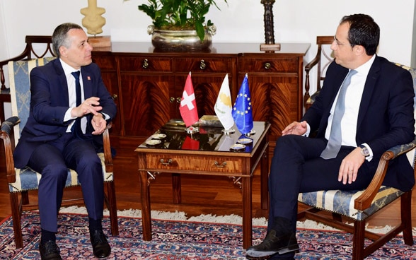 Le conseiller fédéral Cassis et le ministre chypriote des Affaires étrangères Nikos Christodoulides sont assis à une table en bois et discutent.