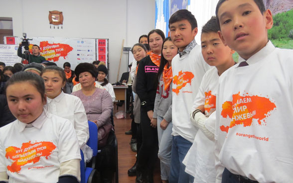 Jungen und Mädchen tragen weisse T-Shirts mit dem orangen 16 Days Kampagnen Logo.
