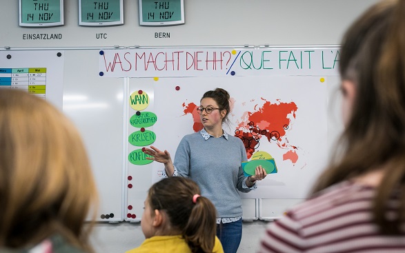 Children listen to a woman presenting the work of Swiss Humanitarian Aid.