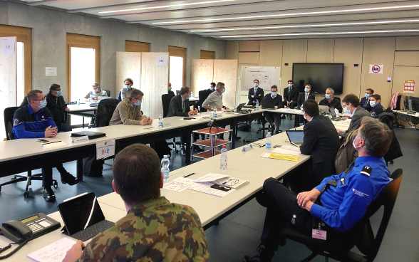 Federal Councillor Cassis sits at a long meeting table with members of the cantonal emergency centre and discusses with them.