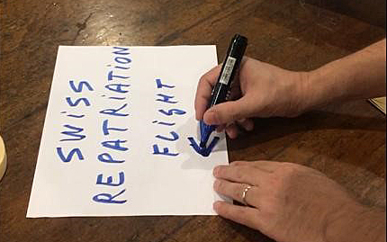 A sheet of paper lies on a table on which "Swiss Repatriation Flight" is written by hand.