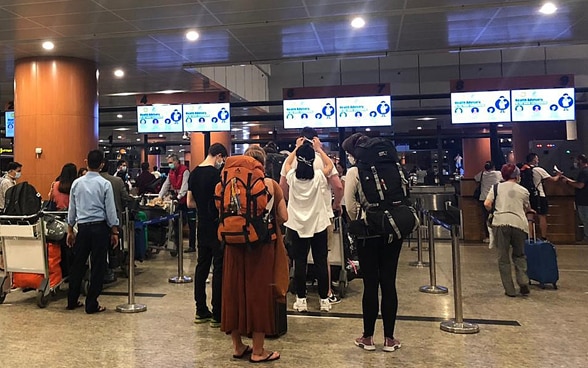 In the hangar of Yangon airport, passengers stand in queues in front of the check-in counters.