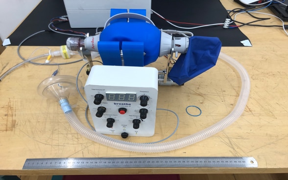 A prototype of a ventilator lies on a workbench.