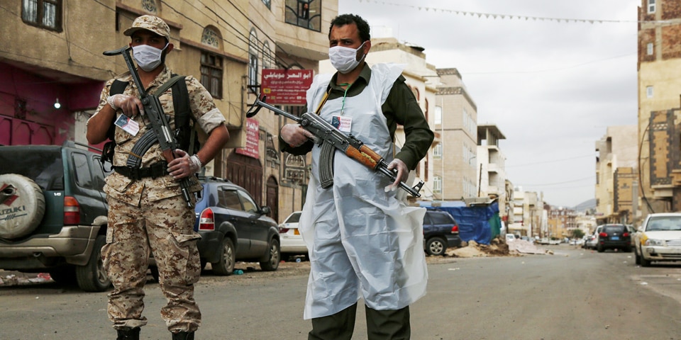 Deux soldats armés contrôlent une rue. Les deux soldats portent des armes à feu et des masques faciaux, l'un d'entre eux porte des vêtements d'hygiène.