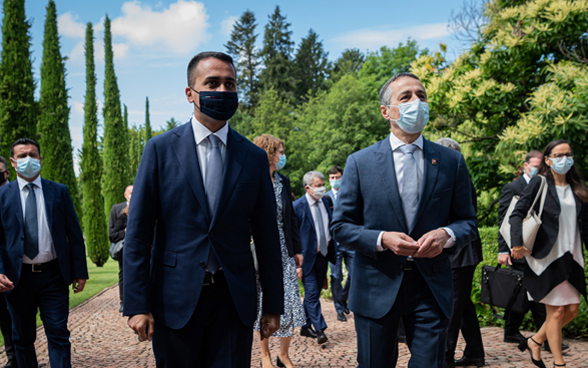 Bundesrat Cassis und der italienische Aussenminister Di Maio spazieren mit ihren Delegationen in einem Park und unterhalten sich. 