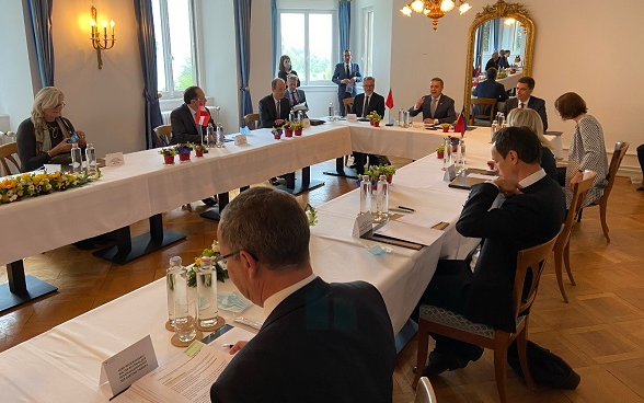 The representatives of the four countries and their delegations gather around a table for discussion.