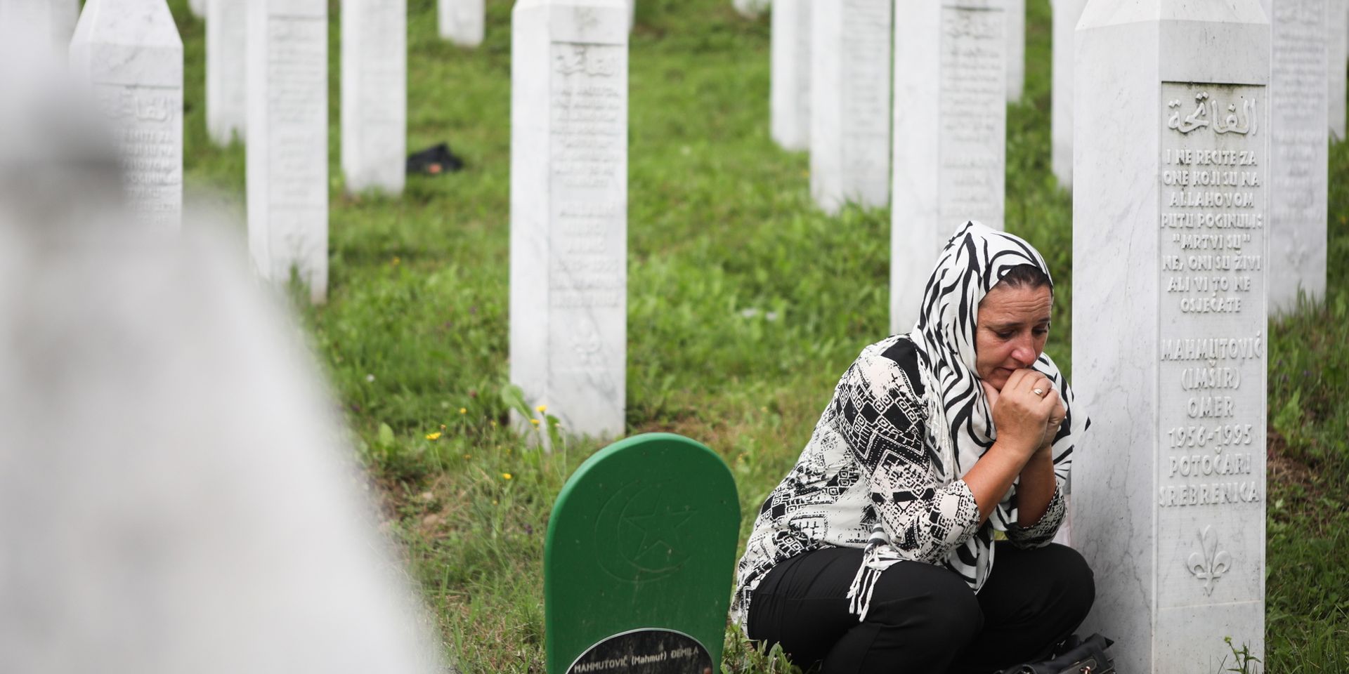 Eine Frau kniet neben einem Gedenkstein auf dem Friedhof in Srebrenica.