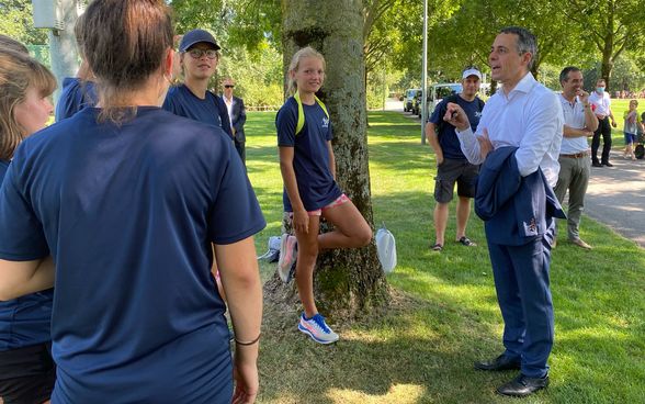 Bundesrat Ignazio Cassis unterhält sich im Freien mit Leichtathletinnen und Leichtathleten.