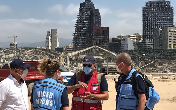 Un membre des groupes d'experts de l'aide humanitaire de la Suisse en discussion avec des experts de l'ONU. En arrière-plan, la ville détruite. 