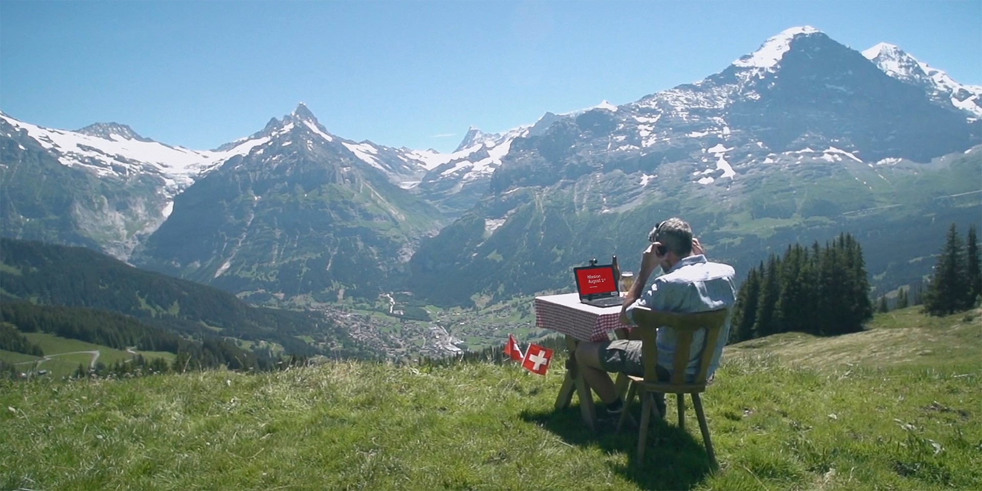 A man is sitting at a table in the Alps, working on a laptop.