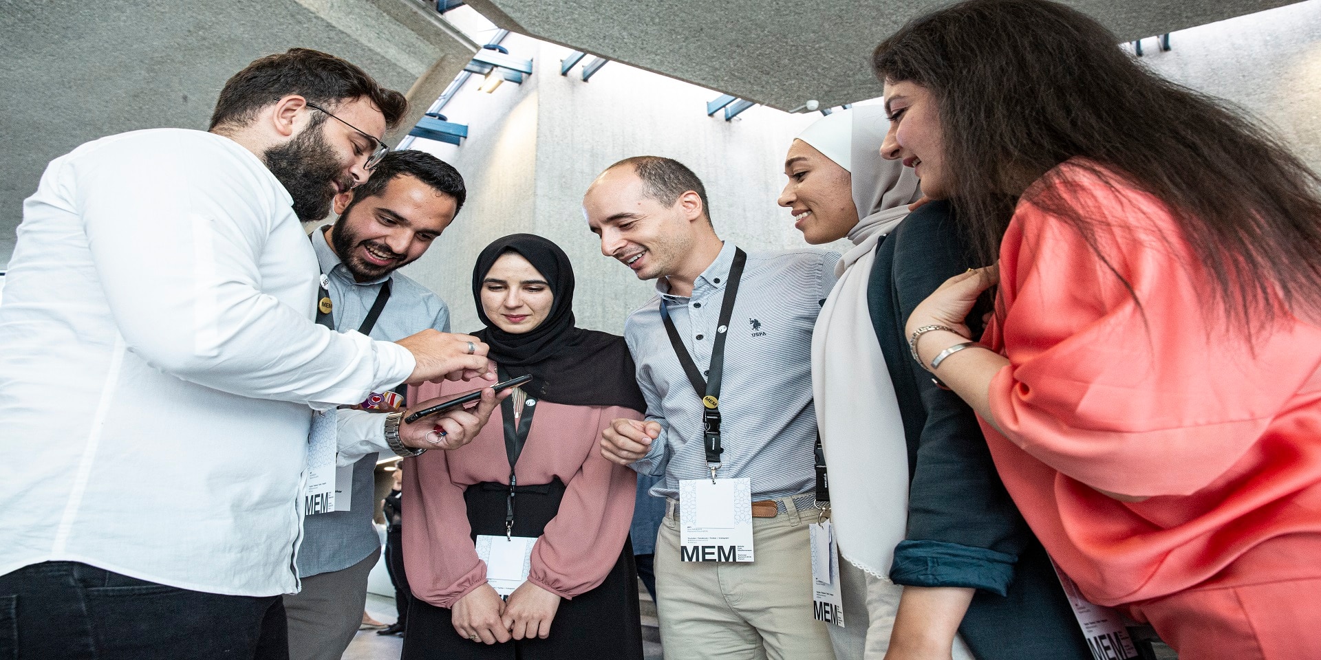 A group of young people, in a semicircle, looking at a phone screen.