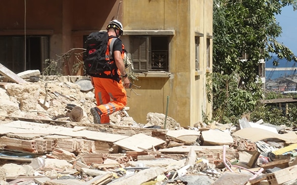 A member of the Swiss Humanitarian Aid Unit walks over the debris of a building.