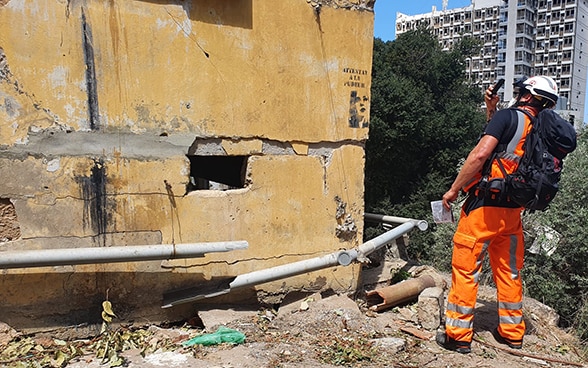 Un expert du Corps suisse d'aide humanitaire prend une photo d'une maison détruite.