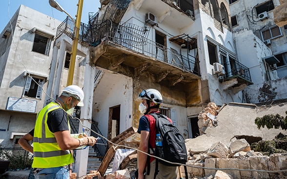 Un expert du Corps suisse d'aide humanitaire est debout avec un expert libanais devant les débris d'une maison.
