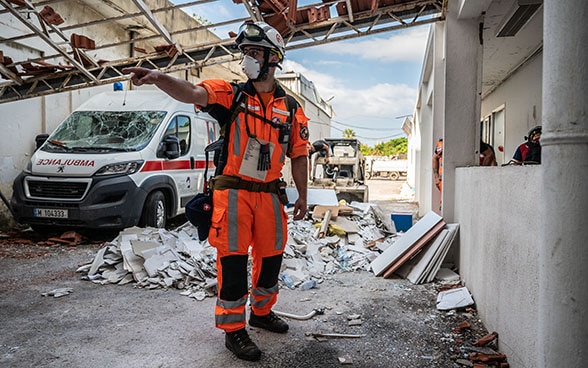 Un expert de l'Aide humanitaire suisse se tient devant les décombres d'un hôpital.