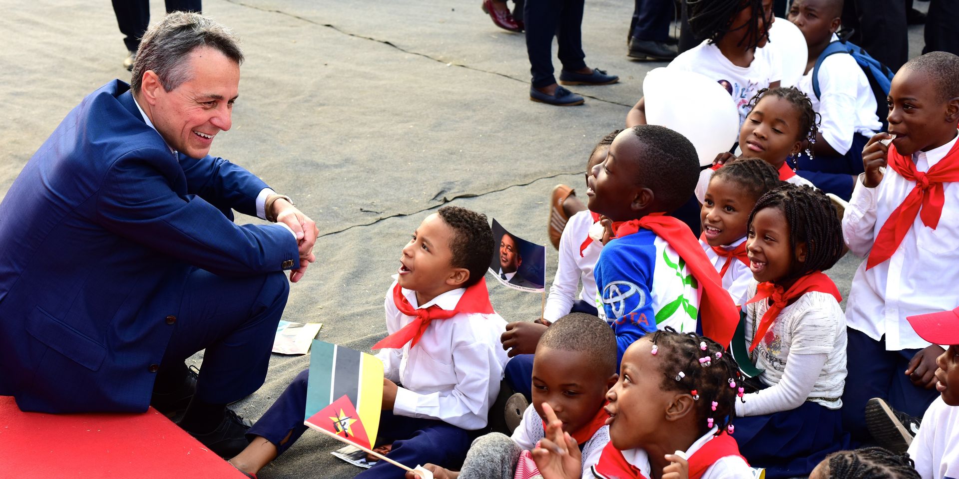 Federal Councillor Ignazio Cassis on his Africa trip smiling as sits on the floor with a group of children.