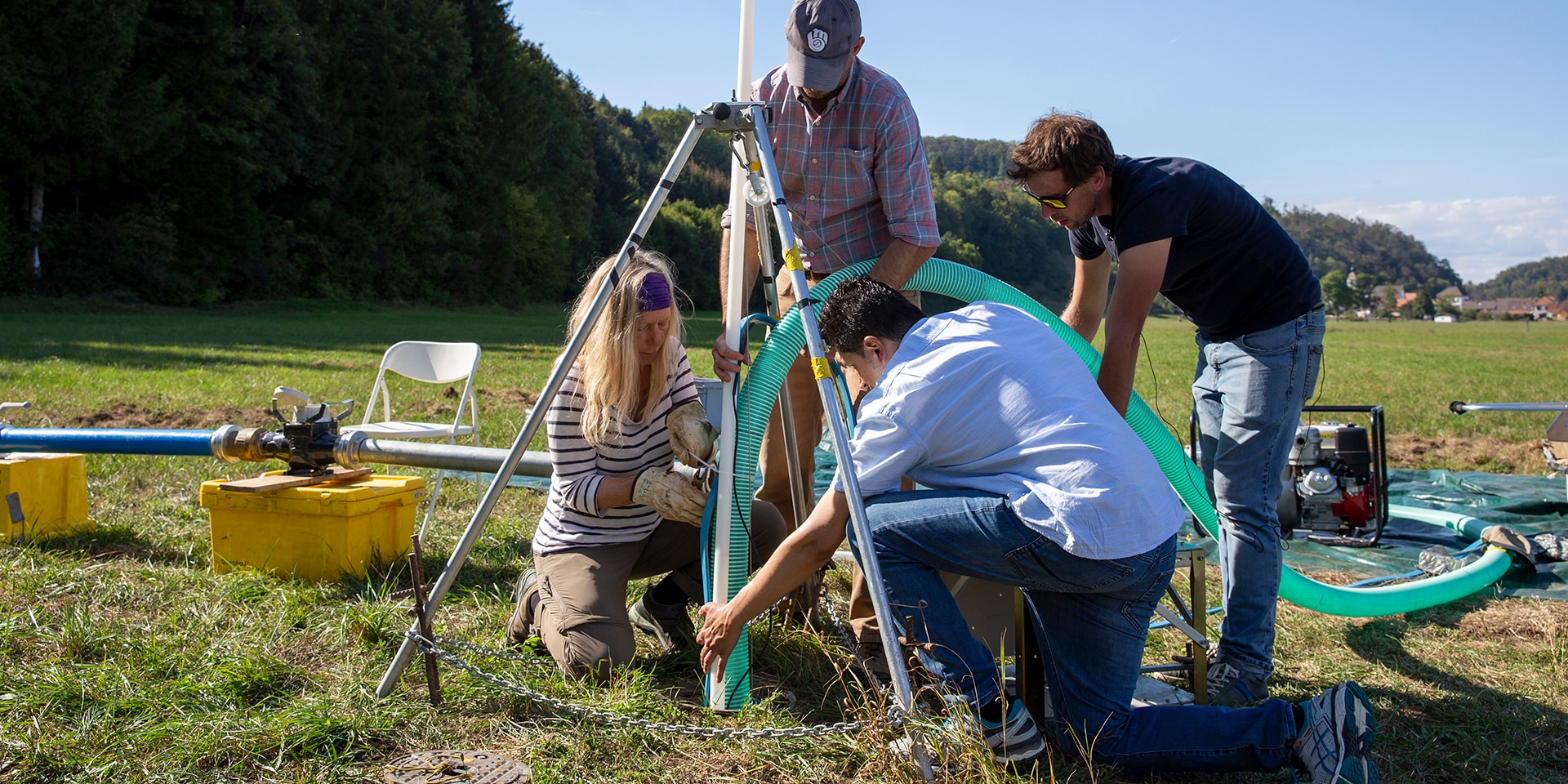 Auf einer Wiese legen vier Experten des Schweizerischen Korps für humanitäre Hilfe (SKH) eine Wasserleitung in ein Erdloch.