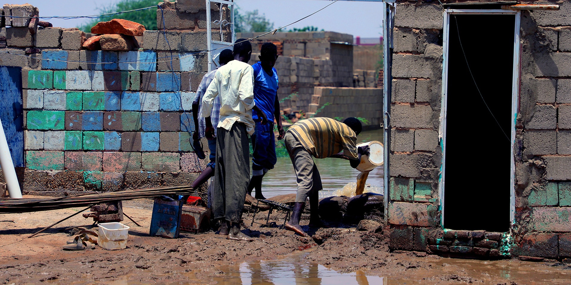 Quatre personnes tentent d’éliminer l’eau et la boue qui se sont introduites dans une habitation gravement touchée par l’inondation.