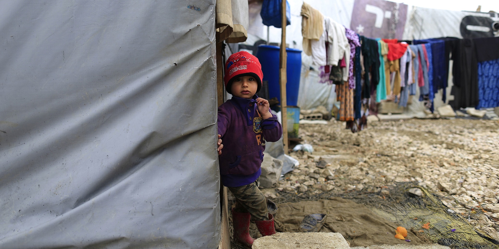 A Syrian refugee boy stands outside his family's tent after heavy rain.