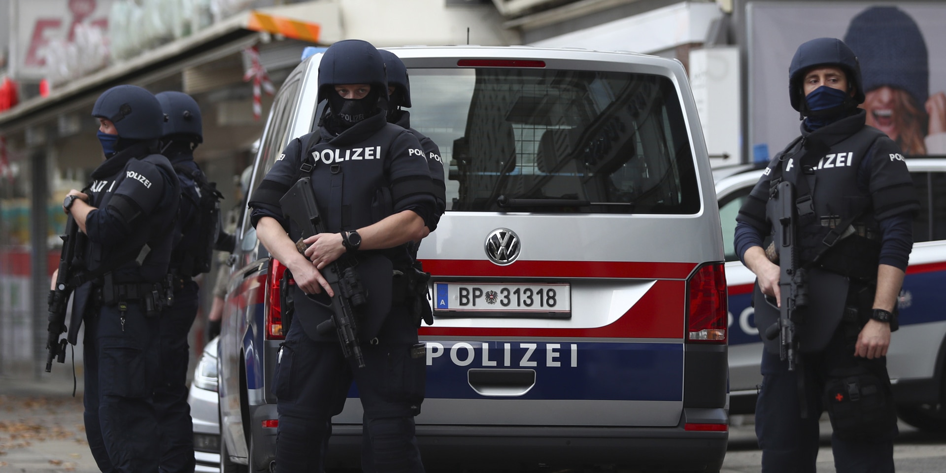 Several heavily armed Austrian police officers stand in front of a police car.