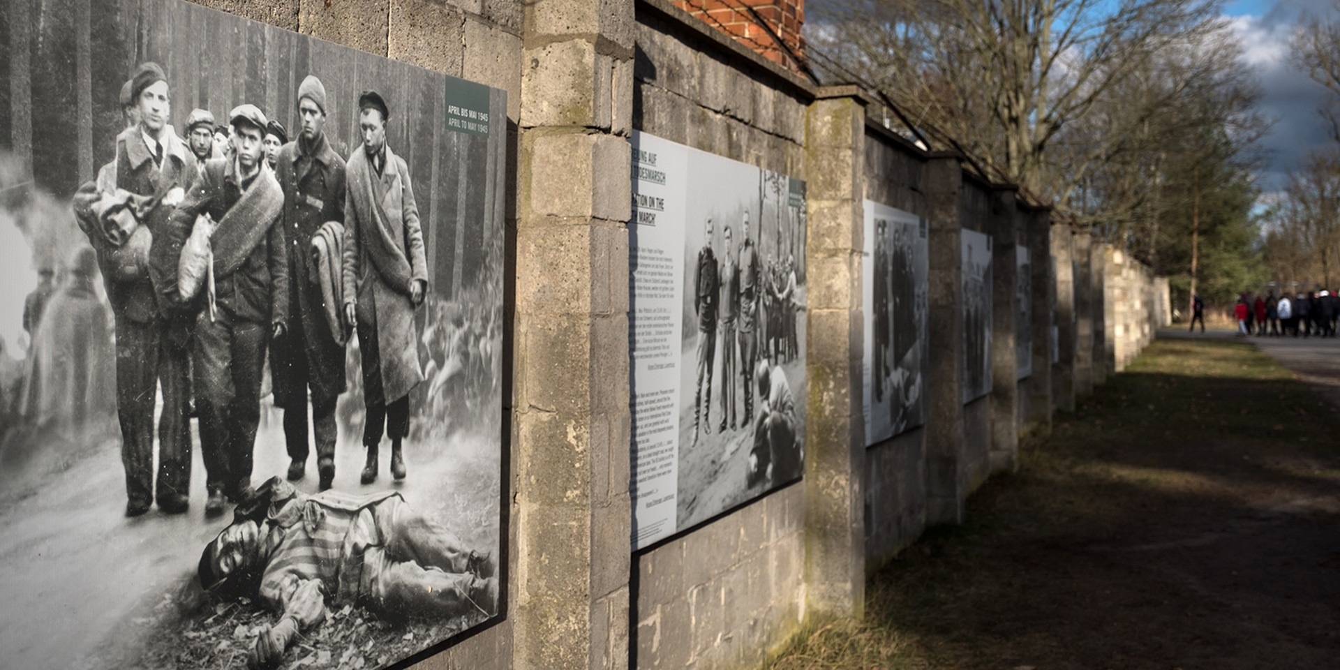 Mauer des ehemaligen Konzentrationslagers Sachsenhausen mit historischen Bildern und Informationstafeln an der Wand.