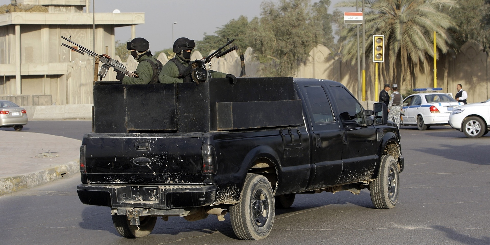 Two masked soldiers from a private security company stand armed to the teeth in the back of a black pick-up truck.