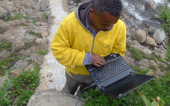  Man standing by a river using a laptop.