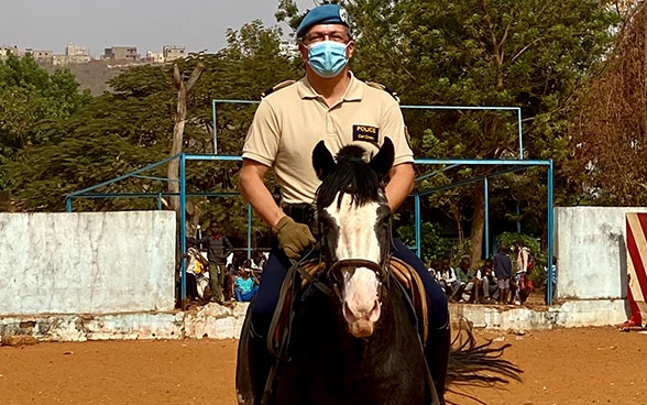 Carl Emery sits in the saddle on a brown horse with his legs in stirrups.