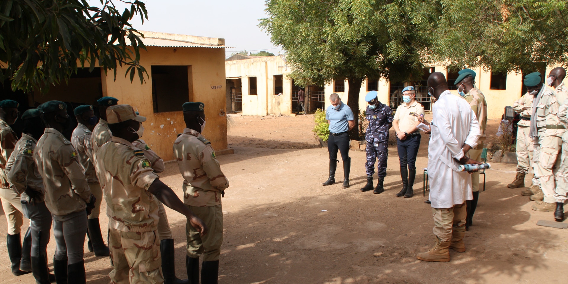 Carl Emery, accompagnato da un comandante della gendarmeria maliana in abito tradizionale, si trova davanti a nove ufficiali in uniforme.