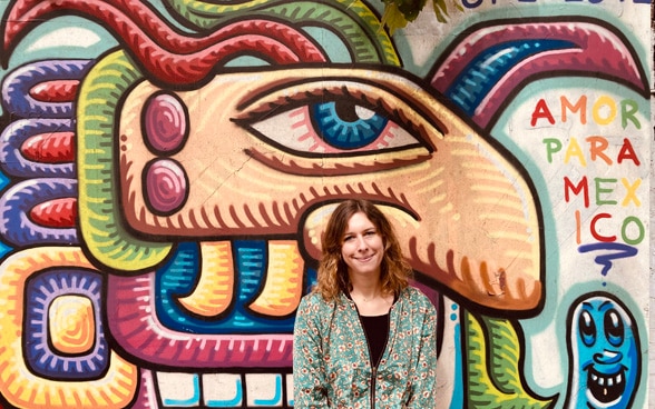Cecilia Neyroud au premier plan. En arrière-plan, une peinture murale colorée de la ville de Mexico.