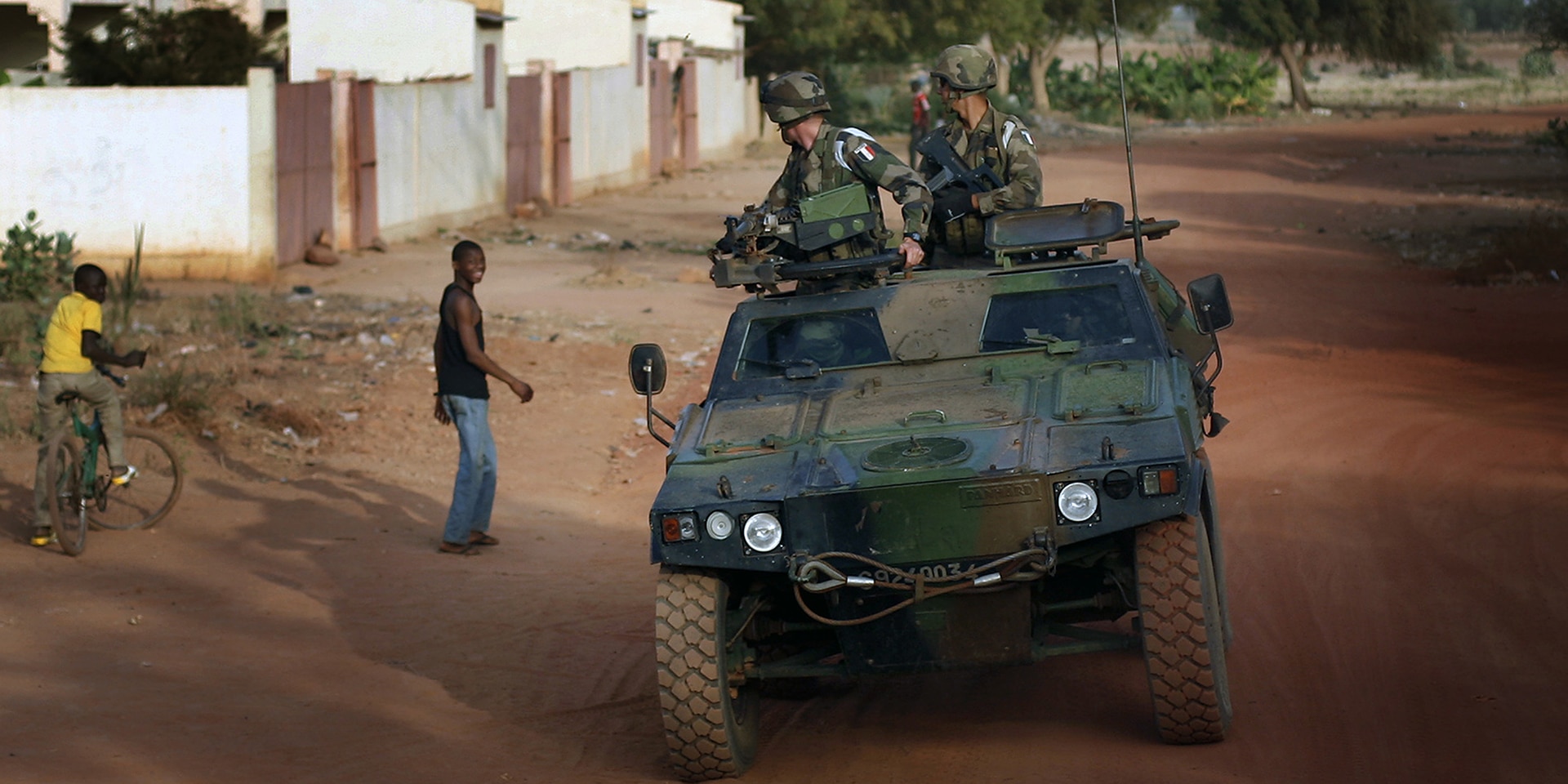 Un véhicule militaire transportant deux soldats passe devant des jeunes hommes dans la région en conflit du Mali.