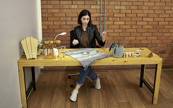 Jeune cheffe d’entreprise irakienne assise à une table en bois en train de fabriquer un bijou.