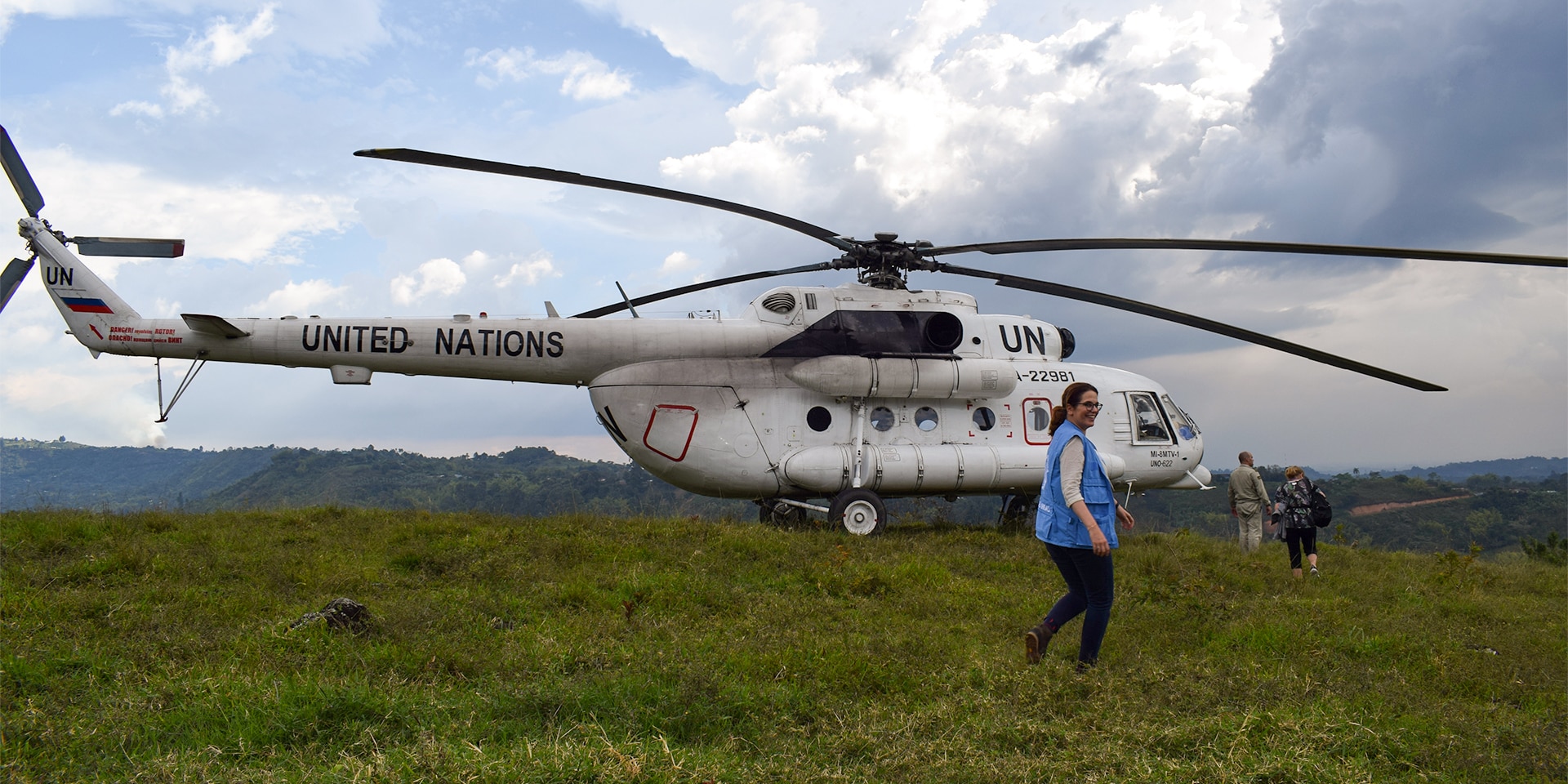 Natalie Kohli devant un hélicoptère de l'ONU posé sur une pelouse verte.