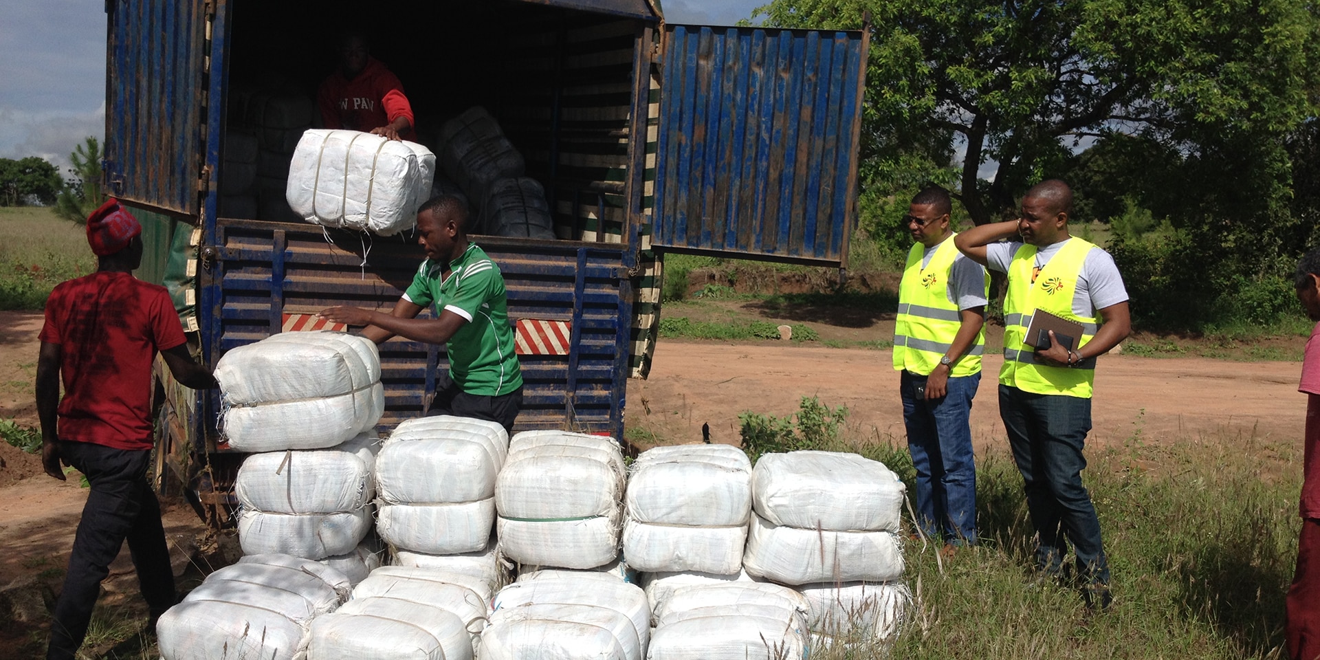 Some men unload white sacks containing mosquito nets from a truck.