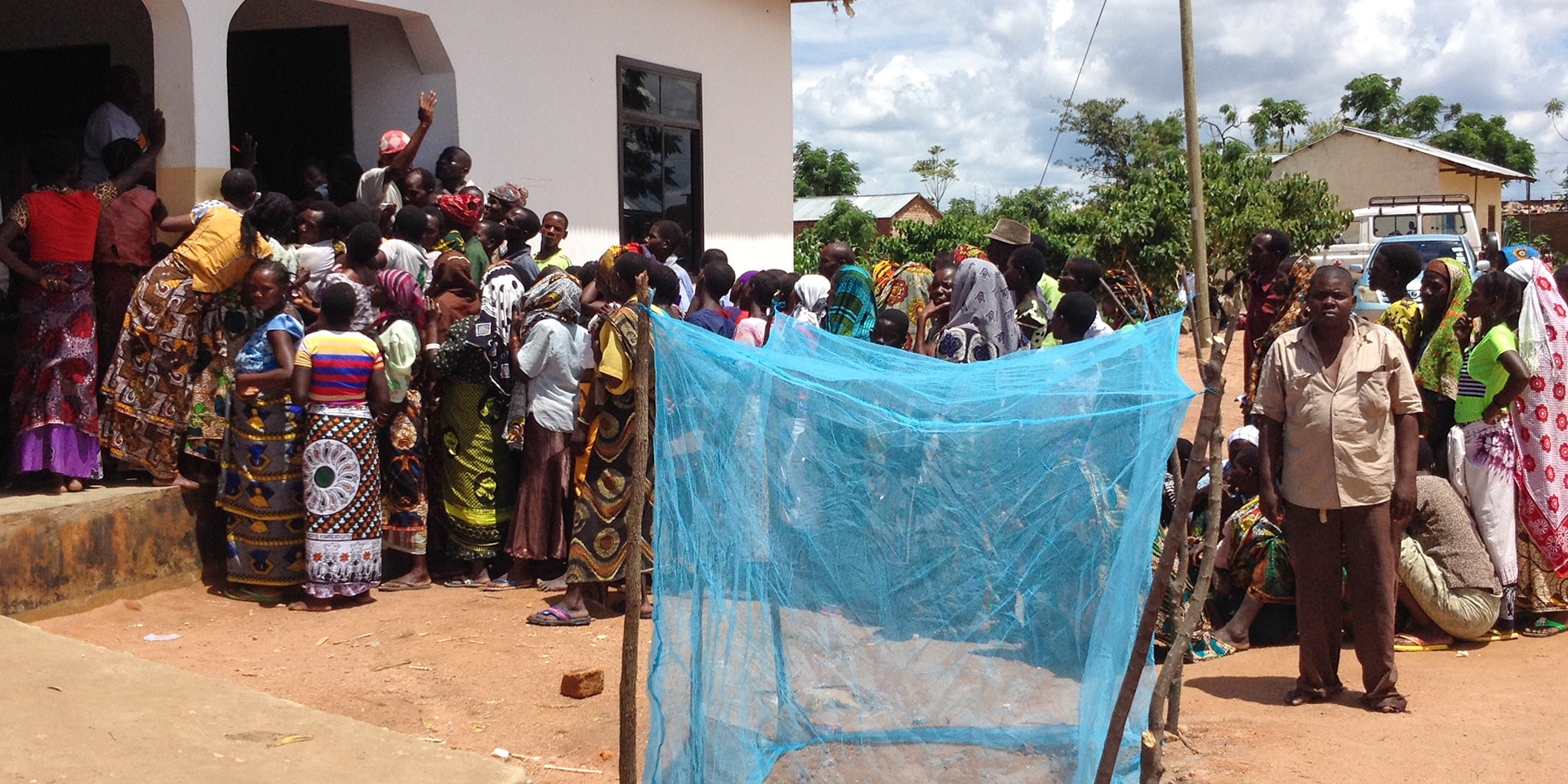 In a village in Tanzania, many people are queuing to collect their mosquito nets. In the foreground, a blue mosquito net.