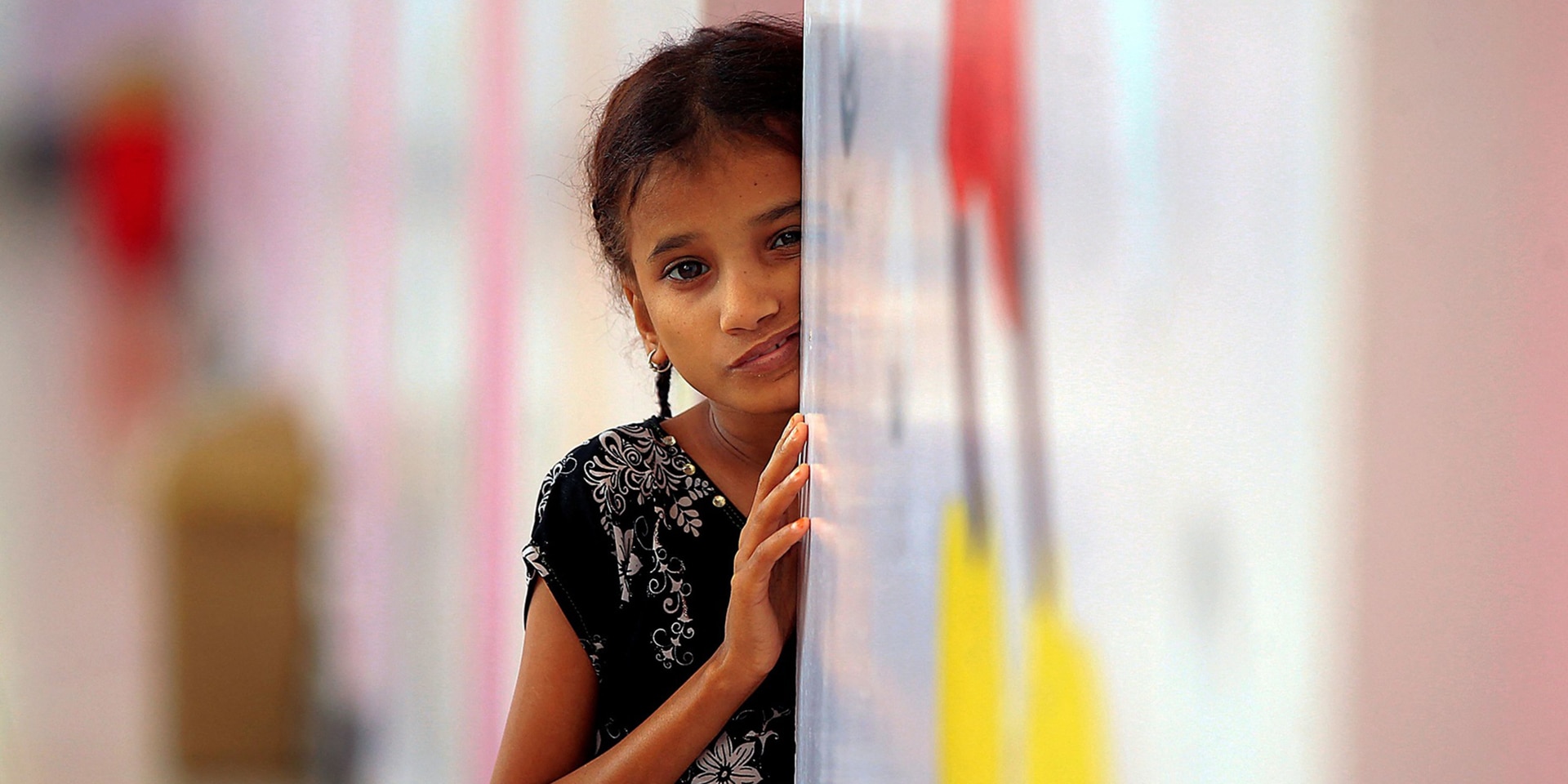 Ein kleines Mädchen lehnt mit besorgtem Gesichtsausdruck an einer Wand und wartet darauf, Essen zu bekommen.