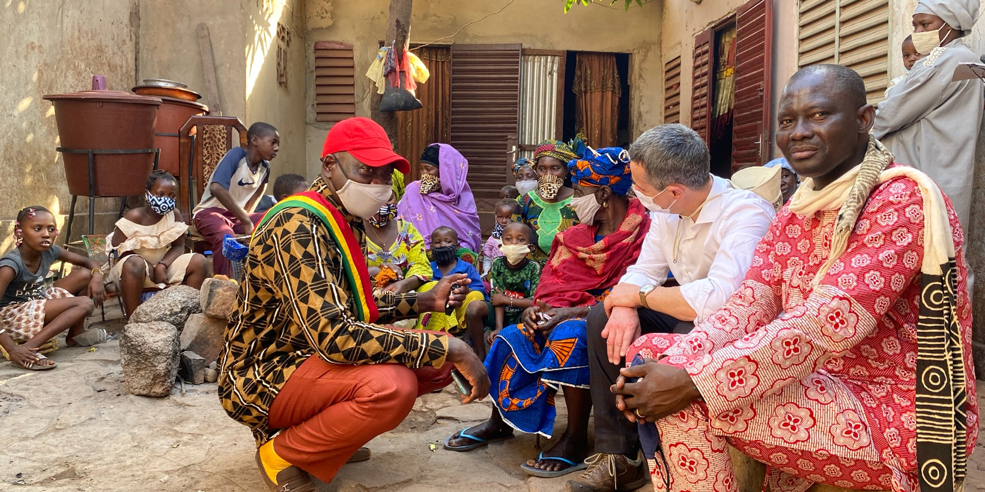 Il ministro degli esteri Cassis è seduto a terra davanti a una casa e sta parlando con alcuni uomini, donne e bambini africani.