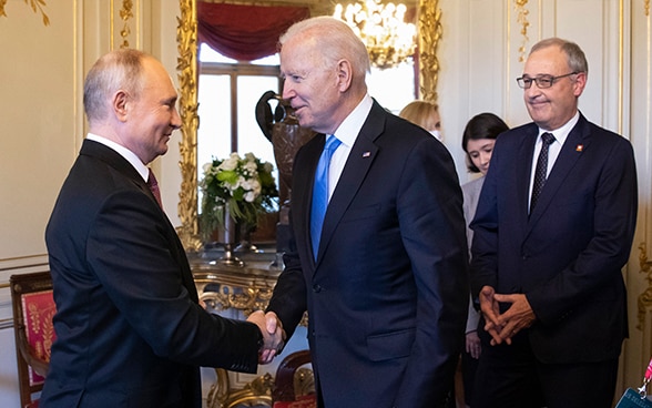 Au premier plan, les présidents des États-Unis et de la Russie se saluent ; à l'arrière-plan, le président suisse Guy Parmelin observe la scène.