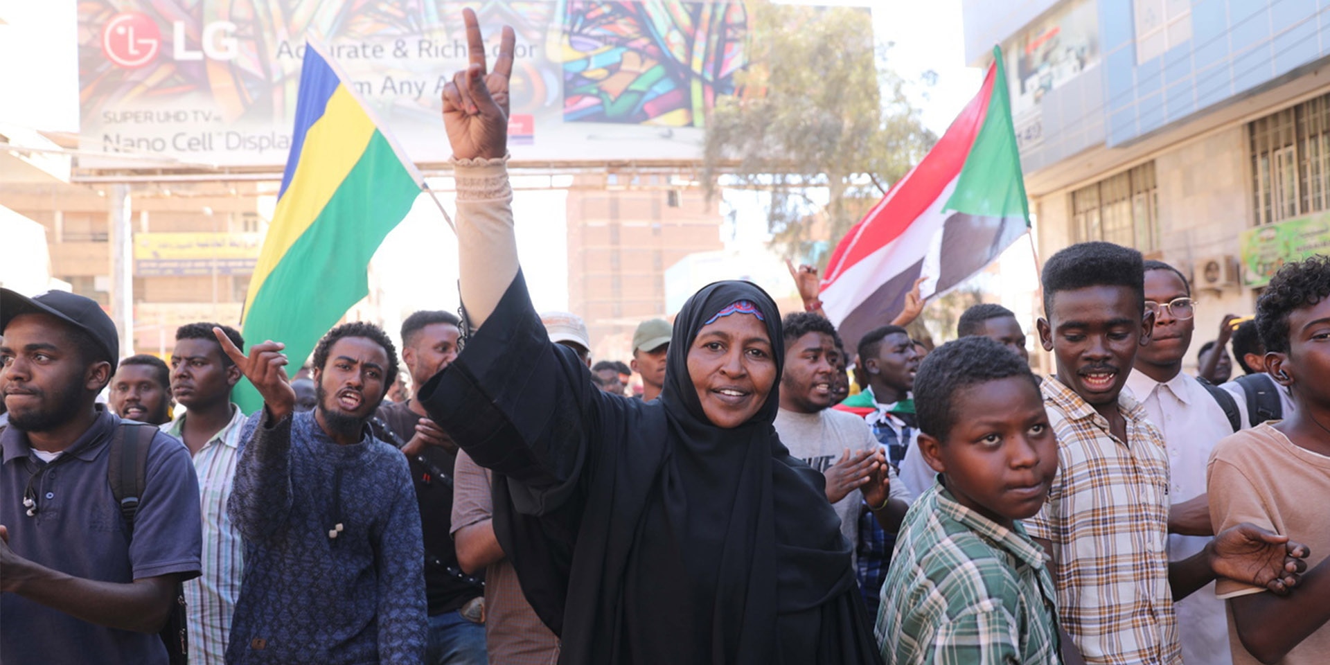 Eine Frau steht in einer Gruppe von Menschen und zeigt das Victory-Zeichen