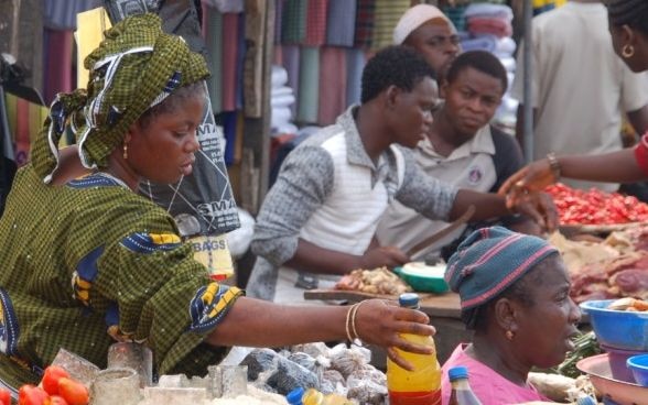 A woman getting a bottle for a customer at a market stall in Africa.