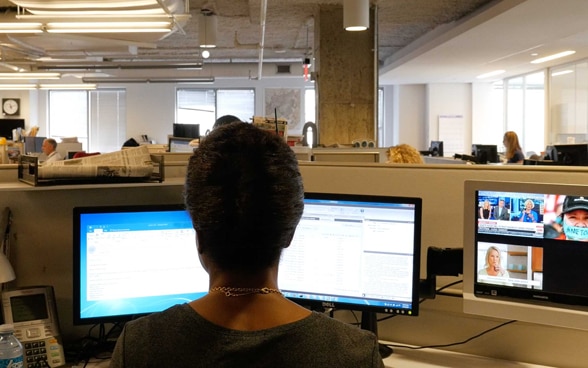 Une journaliste est assise devant son bureau dans une newsroom vide.