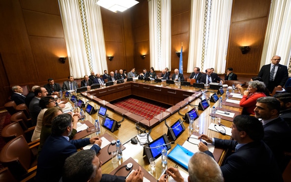 Assis devant des ordinateurs, plusieurs dizaines d’hommes et de femmes discutent autour d’une table de forme carrée.