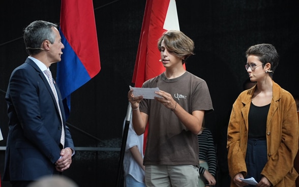 Sul palco, alcune studentesse e alcuni studenti si rivolgono al presidente della Confederazione Ignazio Cassis.