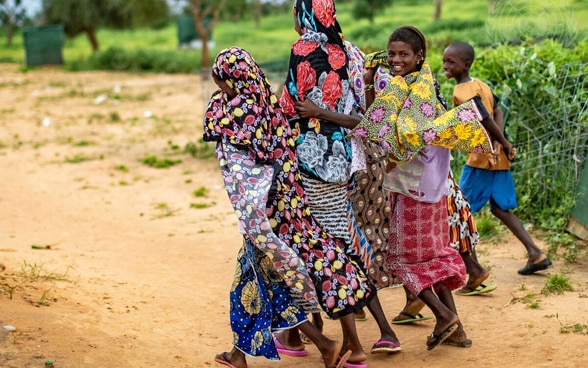 An African woman and children walk along a dusty road.