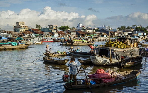 Women steer boats carrying food on the Mekong River. 