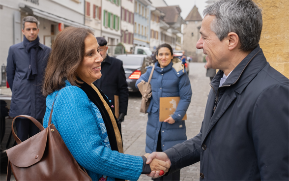 Bundesrat Cassis und Aussenministerin Urrejola Noguera geben sich die Hand. Im Hintergrund sieht man die Häuser von Murten.