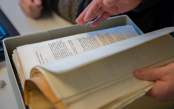 Une personne feuillette des documents qui se trouvent dans une boîte avec ses mains.