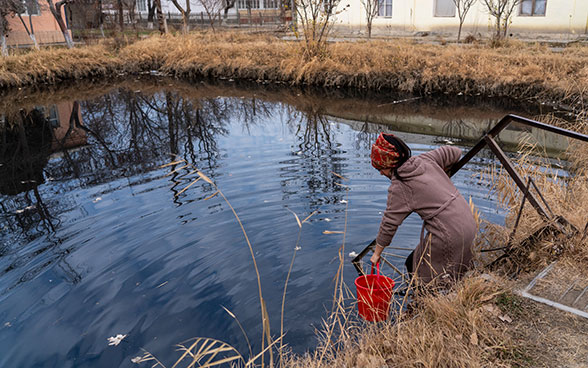 Ein Mädchen, das ein rotes Kopftuch trägt, schöpft mit einem Eimer Wasser.