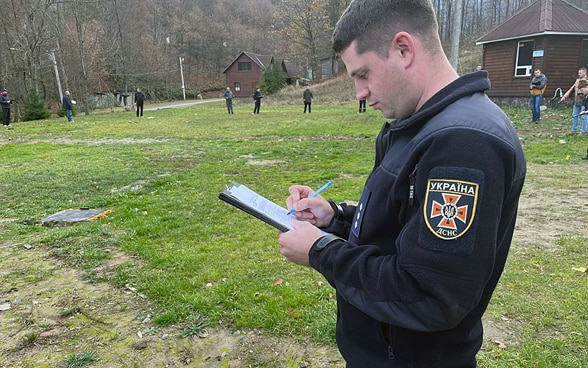 A man standing in a field writing in his notebook.